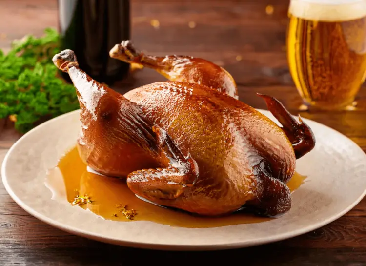 A roast guinea fowl with a glass of beer in the background